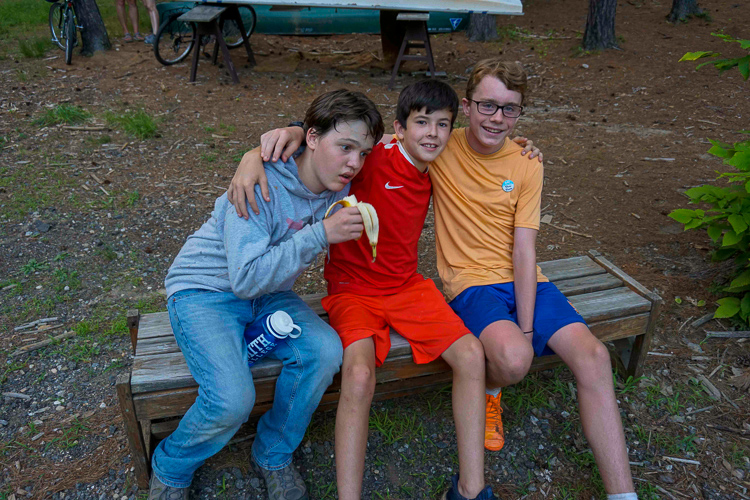 Three boys sitting on a bench smiling with arms around each other