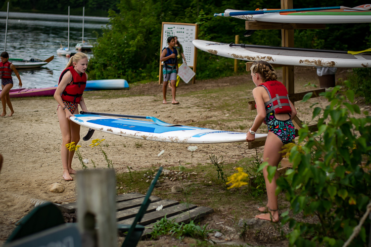 Two campers help each other bring a paddleboard to the water