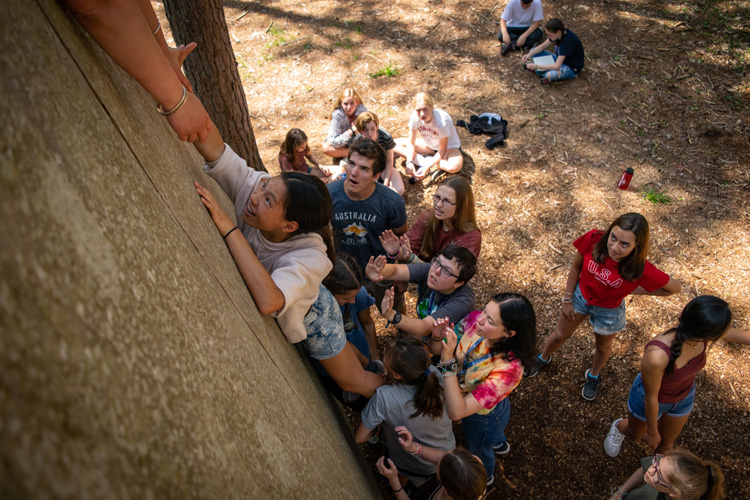 Campers work together to scale the ropes course wall