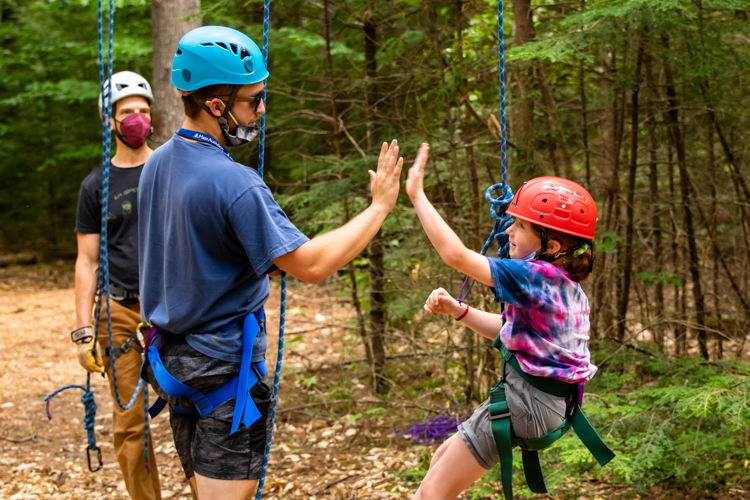 Ropes Course leader Sam gives a camper a high five after she tackled a big challenge on the ropes course