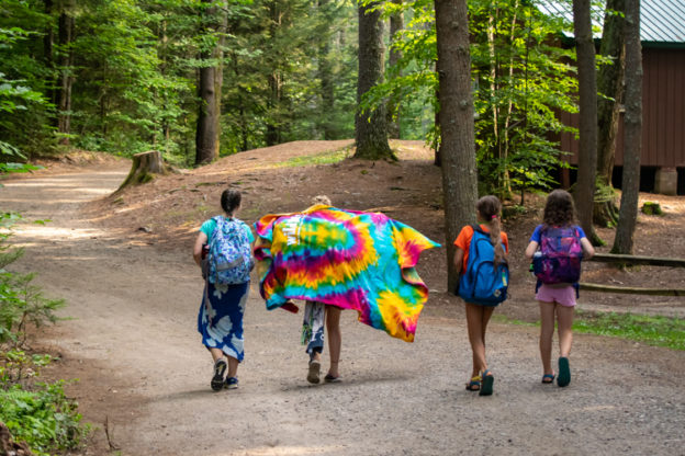 Four campers walking down the road, one carrying a tie-dyed Wildwood blanket