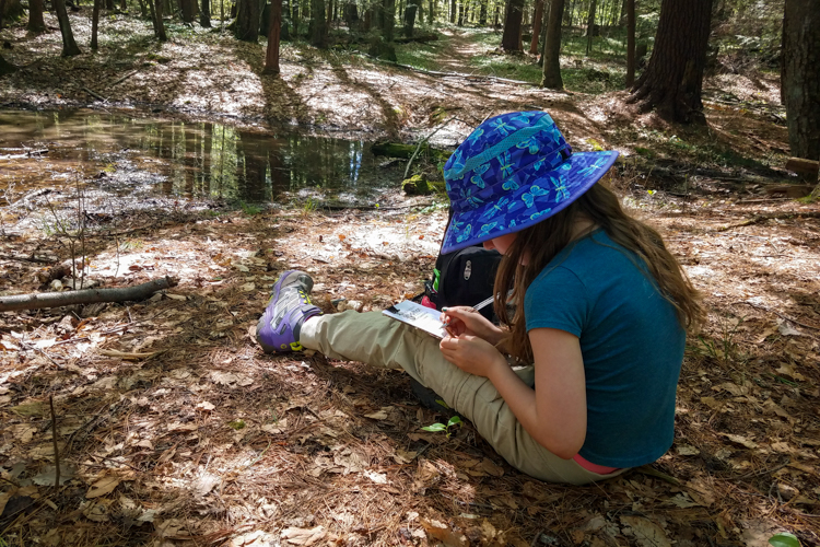 Willow writing in her nature journal beside a vernal pool at Arcadia