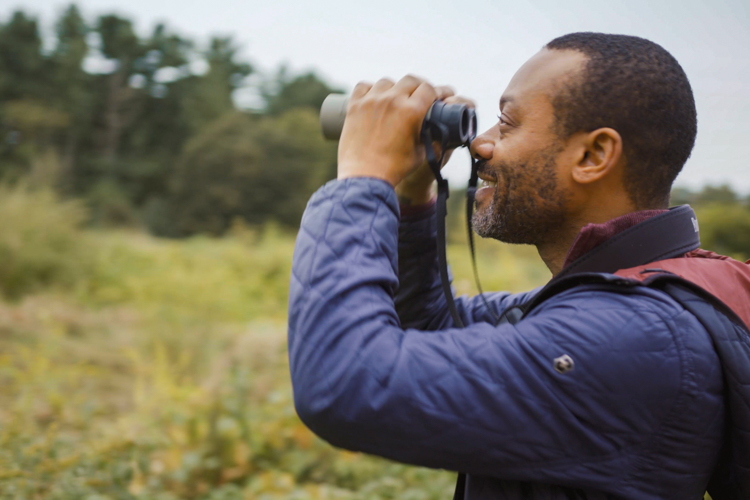 A Black man looking through a pair of binoculars at a wildlife sanctuary