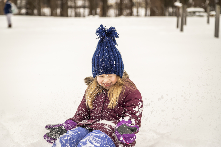 A young girl in winter clothes kneeling in the snow and laughing as she showers herself with snow. Photo © Phil Doyle. Location: Arcadia Wildlife Sanctuary in Northampton & Easthampton