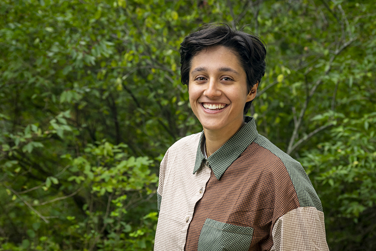 Amara wearing a color-blocked button down, smiling with trees in the background. 