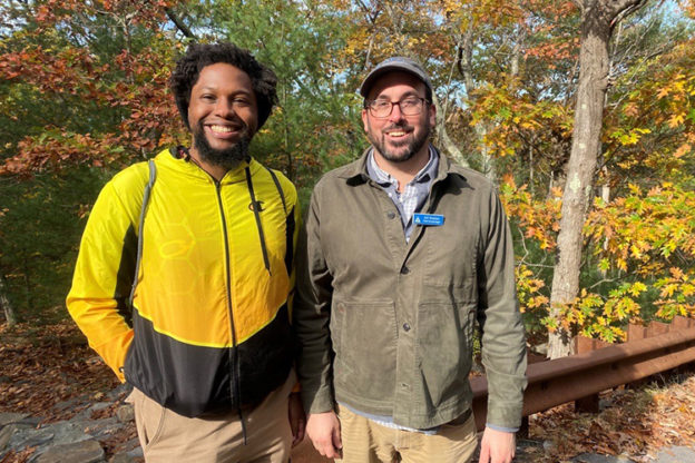 Jovan and his mentor Jeff stand together smiling with fall foliage behind them.