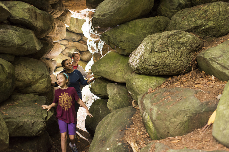 Two adults and a child smile as they pass under a passage made of large rocks.
