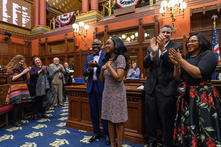 Wawa centered with her hands on her heart as the adults around her clap their hands. 